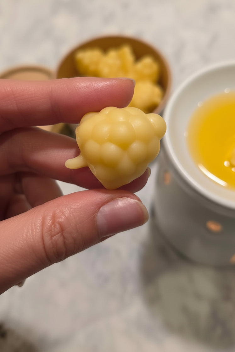 Hand holding a yellow beeswax blackberry-like wax melt with a blurred background