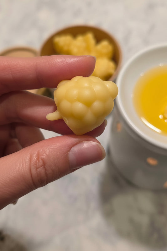 Hand holding a yellow beeswax blackberry-like wax melt with a blurred background